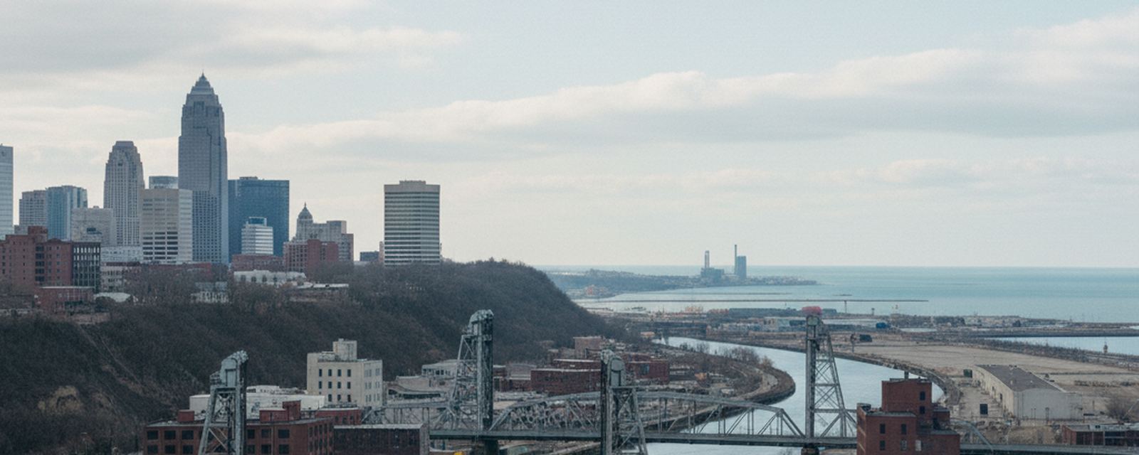 Lift bridges over the Cuyahoga River below the downtown bluff, with the flat lake plain and the open water of Lake Erie beyond the river mouth.