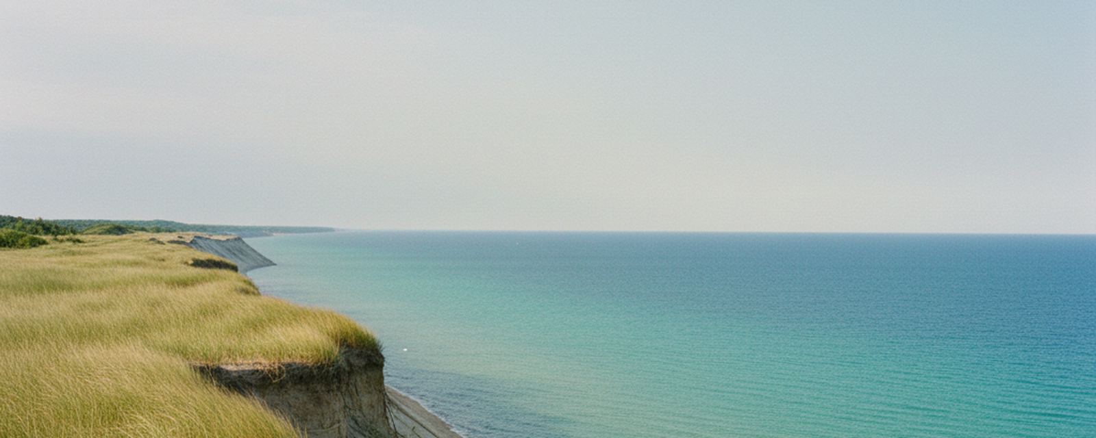 Sand bluffs above Lake Michigan at Sleeping Bear Dunes, beach grass along the rim and open water in bands of green and blue below.